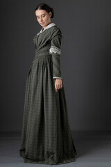 Naklejka premium A Victorian working class woman wearing a checked bodice and skirt and standing alone against a studio backdrop