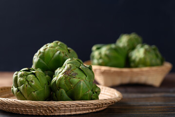 Obraz premium Green artichoke in bamboo basket on wooden background, Edible flower bud