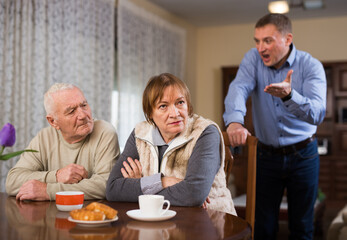 Fototapeta na wymiar Adult annoyed man scolding his senior parents at home