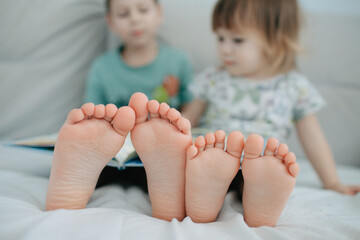 Big brother and little sister holding bare feet close up to camera . Blurred face on background - obrazy, fototapety, plakaty