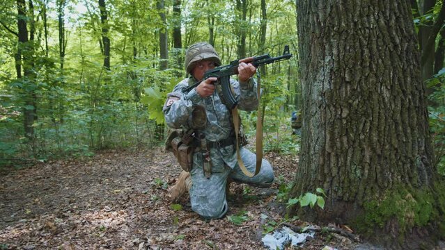 Close up man soldier with fully equipped holds rifle wearing camouflage uniform and helmet attacking enemy. Sitting in position in dense forest