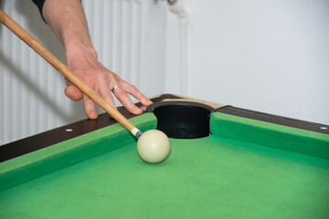 Hand with cue aiming on billiard ball at table

