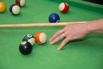 Hand with cue aiming on billiard ball at table

