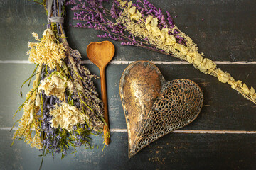 Cooking concept: Close-up of a heart shaped wooden spoon arranged between different flowers on a dark background
