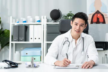 Portrait of Asian doctor sit on table in hospital and look at camera.