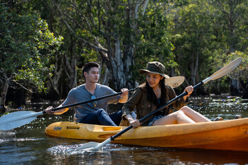 Asian attractive romantic young couple rowing kayak in a forest lake.