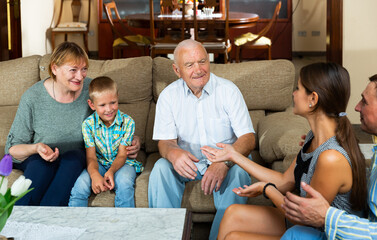 Happy grandparents receiving children and preteen grandson at home, cheerfully talking on sofa