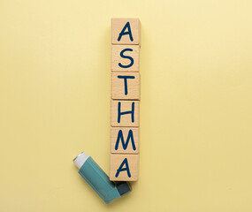 Word ASTHMA made of cubes and inhaler on color background