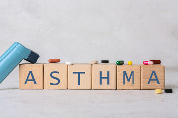 Word ASTHMA made of cubes, inhaler and pills on light background