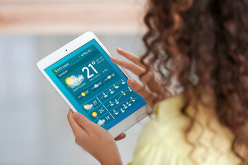 Young woman with tablet computer using weather forecast application at home - obrazy, fototapety, plakaty