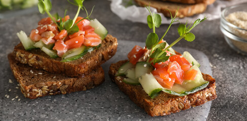 Tasty bruschettas with cucumber and salmon on grunge background, closeup