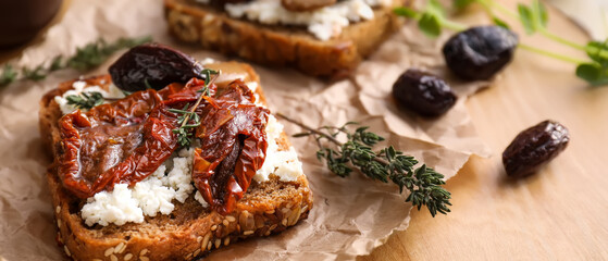 Tasty bruschetta with cheese, sun-dried tomatoes and olives on wooden board