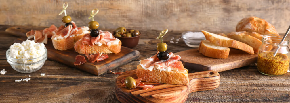 Tasty bruschettas with cheese, prosciutto and olives on wooden background