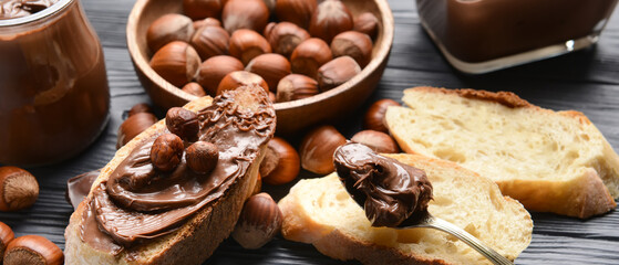 Pieces of bread with tasty chocolate butter and hazelnuts on table