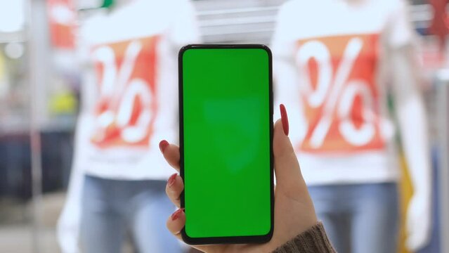 Big sale. Lots of discount coupons to save money on your smartphone. A girl is holding a phone with a green screen in a shopping center. black Friday.