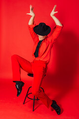 Tall handsome man dressed in red shirt, trousers and black hat posing on the red background