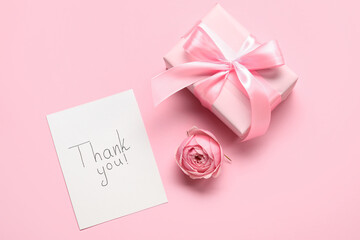 Sheet of paper with text THANK YOU, gift box and flower on pink background