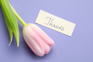 Sheet of paper with word THANKS and flower on purple background
