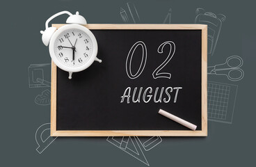 august 2. 2th day of month, calendar date.   Blackboard with piece of chalk and white alarm clock on green background. Concept of day of year, time planner, summer month