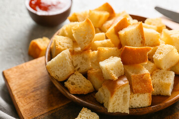 Bowl with tasty croutons on wooden chopping board, closeup