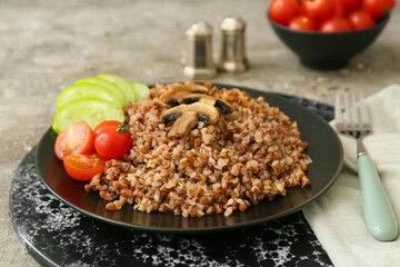 Plate of tasty buckwheat porridge with vegetables and mushrooms on grey table
