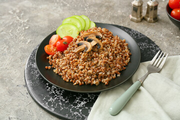 Plate of tasty buckwheat porridge with vegetables and mushrooms on grey table