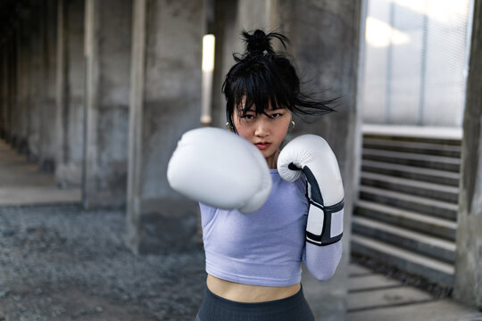 Portrait of sporty female athlete wearing boxing gloves outdoors.