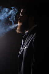 Cigarette smoke on black background. Businessman in suit smoking cigarette.