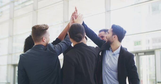 The best in the business. Successful group of business people celebrating and giving a high five while standing together in a modern office. Motivated colleagues winning after achieving their goals
