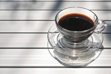 transparent cup of black coffee on the stainless steel table with the shade of tree's shadow