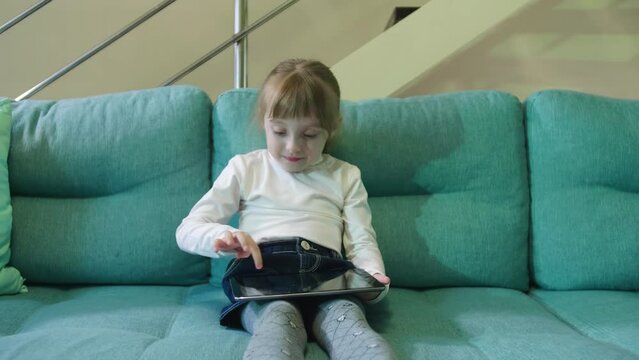 Small Child Hold Pad Computer Surfing Internet Play Game At Home Alone. Preschooler Girl Sitting On Sofa Surfing Internet Watching Video Internet Education Concept