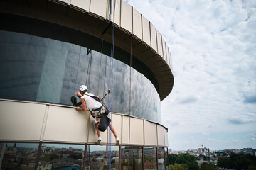 Industrial mountaineering worker professional cleaner hanging on climbing rope and cleaning window...