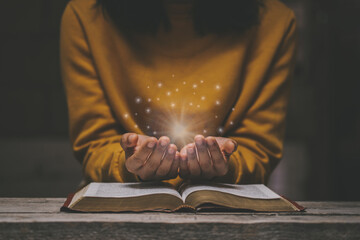 Woman praying on holy bible in the morning have a Yellow lights and sparkles coming. Woman hand...
