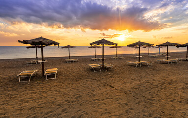  empty beach during beautiful sunrise or sunset with chaise loungues and nice umbrellas with blue sea