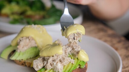 With a fork, they pick up a delicious dressing from a sandwich with fresh avocado and sauce. White plate with vegetarian sandwiches on the table in the restaurant. Healthy avocado sandwiches.