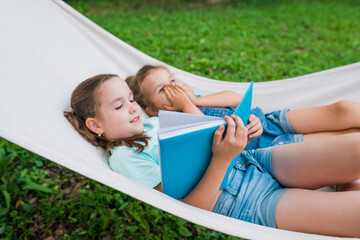 Girls lying in  hammock and reading a book in the garden. Friendship and childhood. Outdoor...