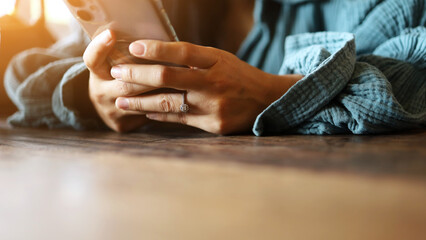 A woman's hand is typing text messages, chatting via apps, or searching for information on a smartphone on a wooden table in a restaurant or café on weekends.