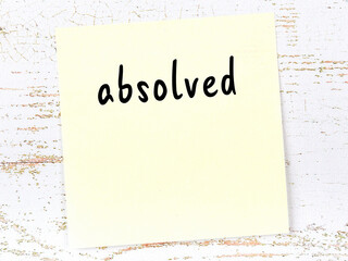 Yellow sticky note on wooden wall with handwritten word absolved