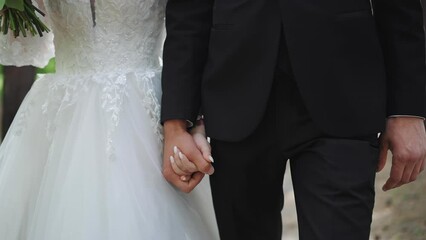 Wife in stylish dress and husband in suit walk joining hands along park closeup. Loving couple at wedding ceremony. Happy matrimonial event