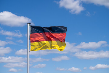 National flag of Germany waving in strong wind against blue sky with scattered white clouds