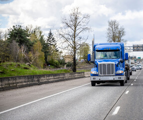Blue low profile cab big rig semi truck transporting cargo on flat bed semi trailer running on the wide highway road