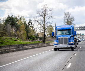Fototapeta na wymiar Blue low profile cab big rig semi truck transporting cargo on flat bed semi trailer running on the wide highway road