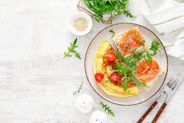 Omelette or omelet, fresh arugula and tomato salad and toasts with butter and salted salmon, top view