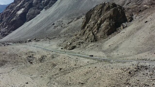 aerial drone of a fast moving motorcycle driving on a road in the desolate empty roads of Skardu Pakistan overlooking the mountains and cliffs on a sunny summer day.