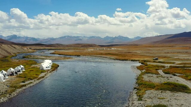 Aerial drone flying past luxury glamping tents along an empty natural river in the high-altitude alpine plain of Deosai National Park located between Skardu and Astore Valley in Pakistan while sunny