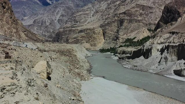 aerial drone flying over a mountain cliff towards the fast flowing gray Indus River in Skardu Pakistan overlooking the large mountains during a sunny summer day