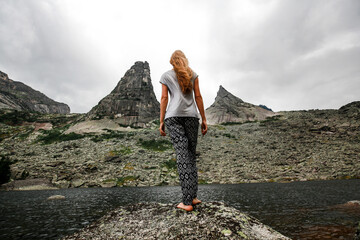 A woman barefoot looks at a lake and mountains of unusual shape. A parabola. Cloudy weather. The concept of travel. Ergaki, Russia.