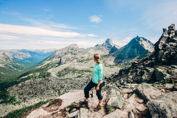 Fototapeta premium Girl on mountain peak with looking at beautiful mountain valley. Landscape with sporty young woman, blue sky and sunny day. Travel and tourism. Hiking
