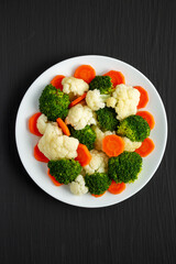 Mixed Organic Steamed Vegetables (Carrots, Broccoli and Cauliflower) on a Plate on a black background, top view. Flat lay, overhead, from above.