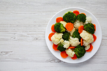 Mixed Organic Steamed Vegetables (Carrots, Broccoli and Cauliflower) on a Plate on a white wooden background, top view. Flat lay, overhead, from above. Copy space.